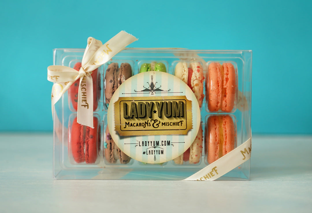 Ten of Lady Yum's June flavors in a clear box, with ribbon and sticker. The macarons shown left to right are Rainbow Nerds, Chubby Hubby, Key Lime Pie, Strawberry Shortcake and Peach Almond Prosecco