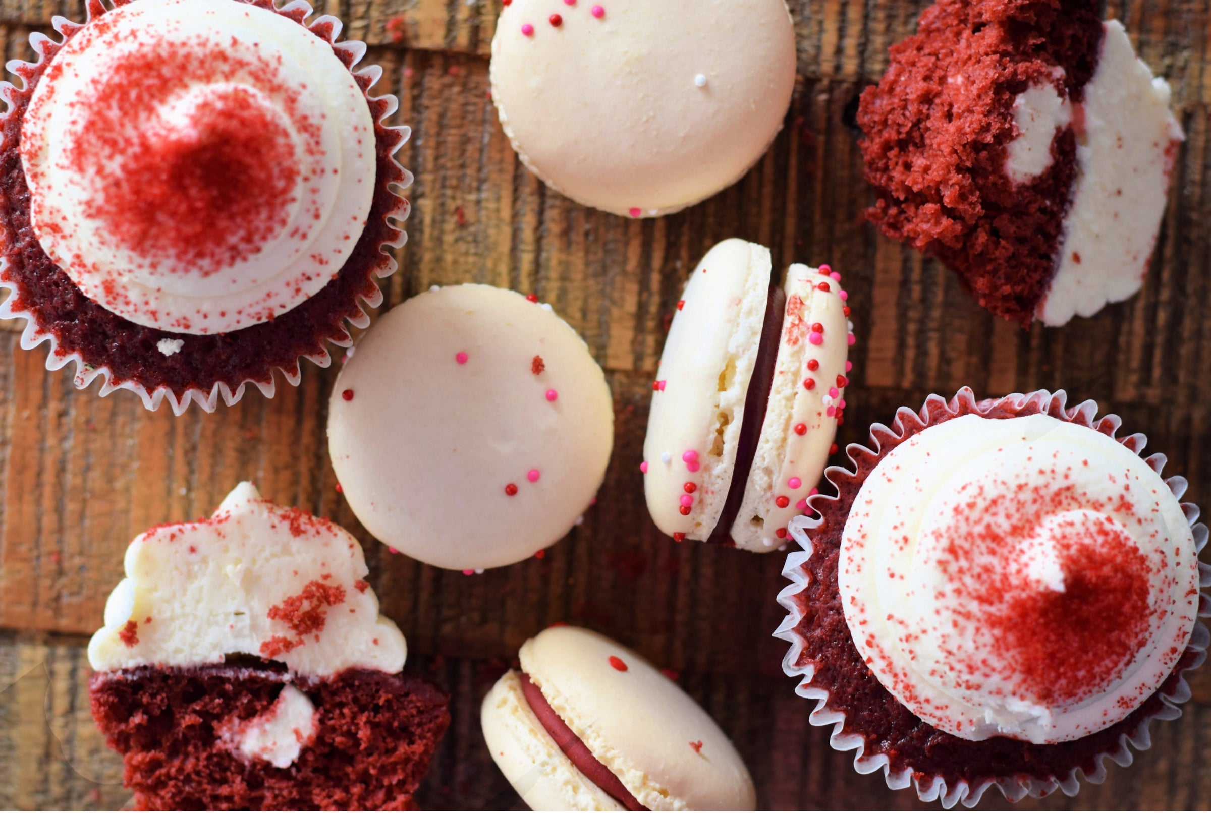 Assorted red velvet cupcakes and macarons on a wooden surface